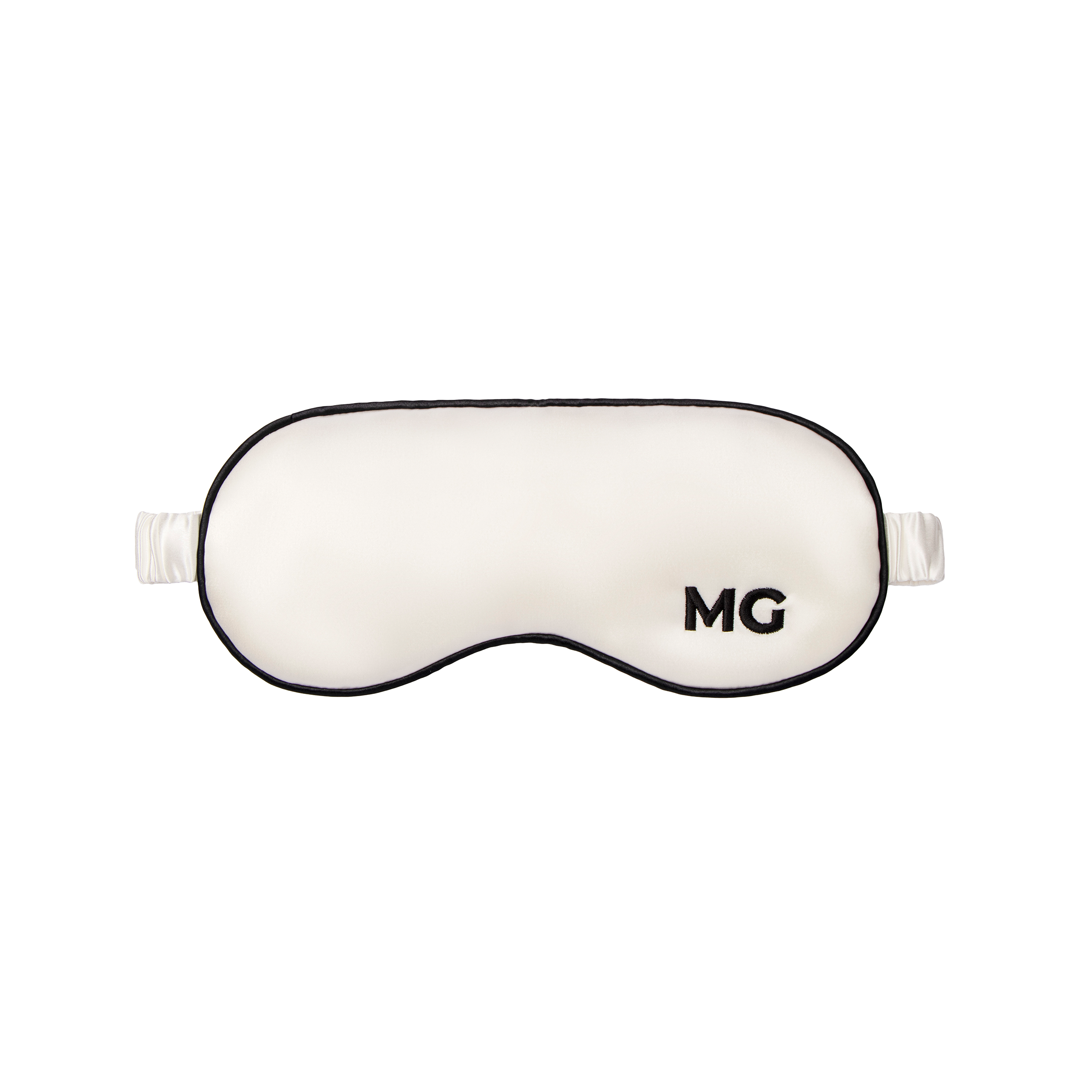 A white silk sleep mask with the initials 'MG' embroidered on the front.