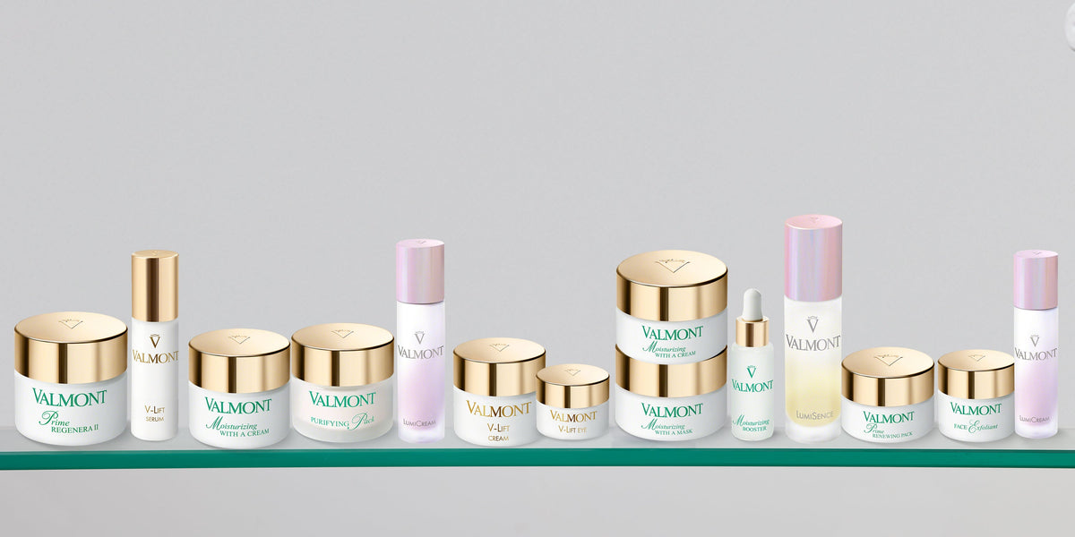Valmont skincare jars and bottles with gold and pale pink details on a glass shelf