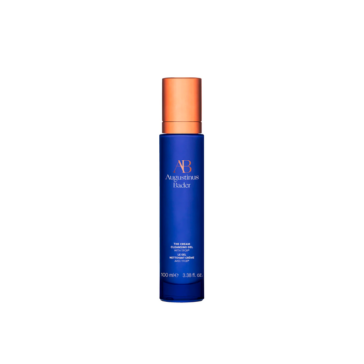 A blue pump bottle of Augustinus Bader The Cream Cleansing Gel with orange accents on the cap.