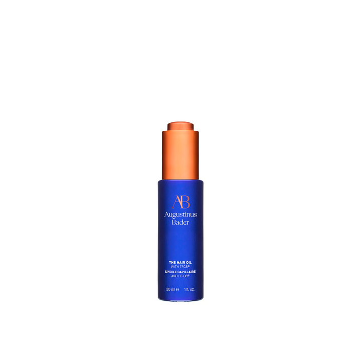 A bottle of Augustinus Bader The Hair Oil with a blue label and orange cap.