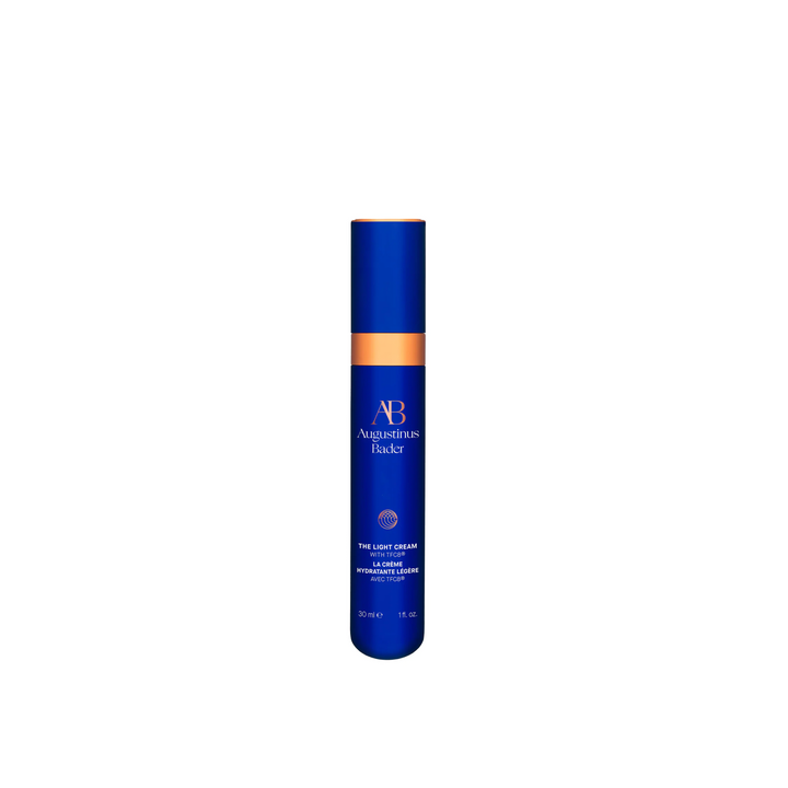A bottle of Augustinus Bader The Light Cream, with a blue and orange design, standing upright.