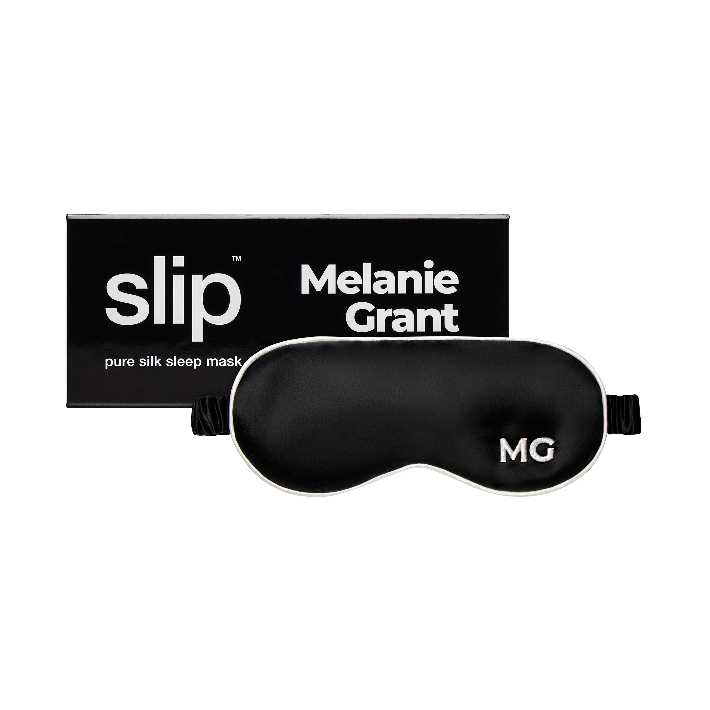 A black silk sleep mask with the initials 'MG' embroidered on the front, next to the box it comes in