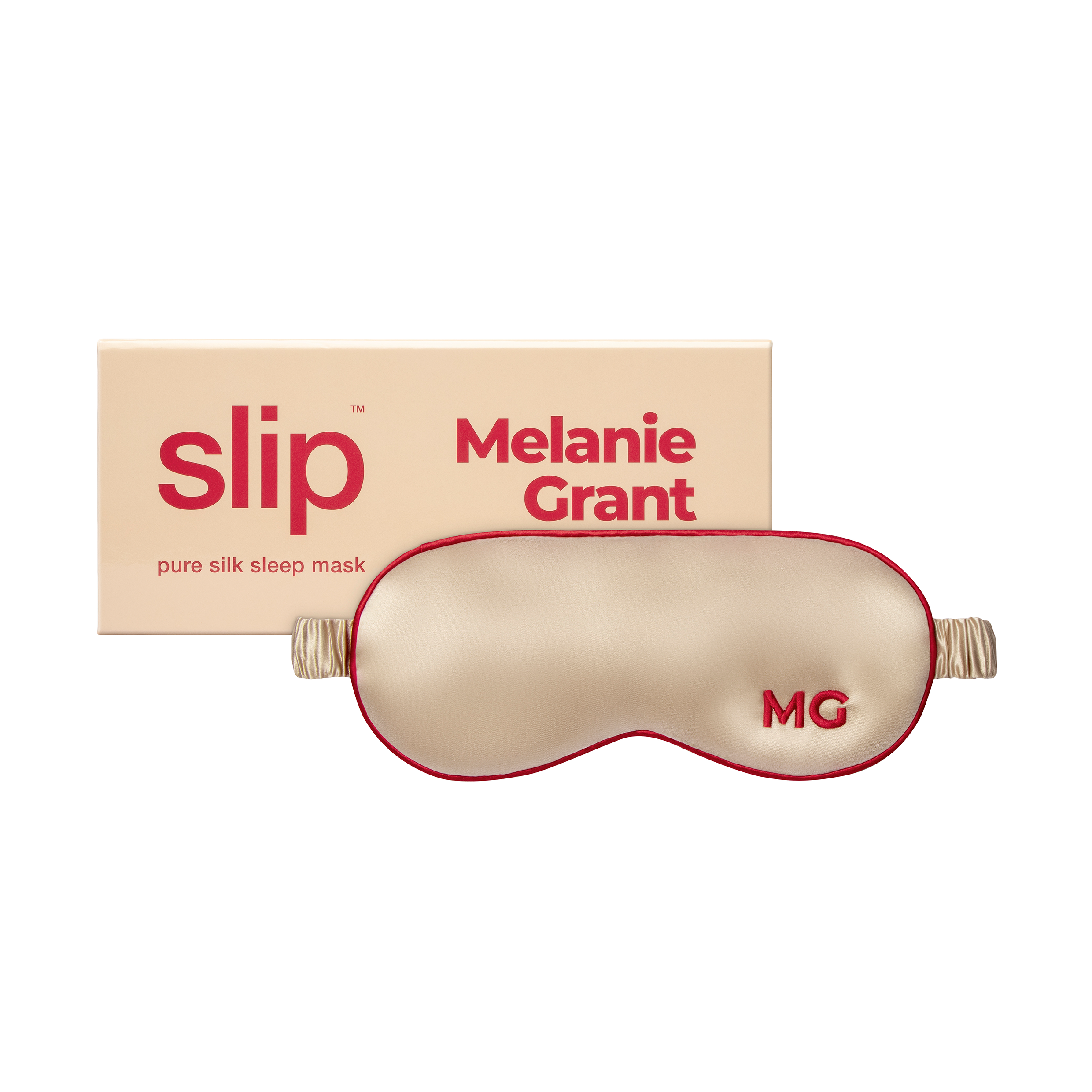 A champagne silk sleep mask with the initials 'MG' embroidered on the front, next to the box it comes in
