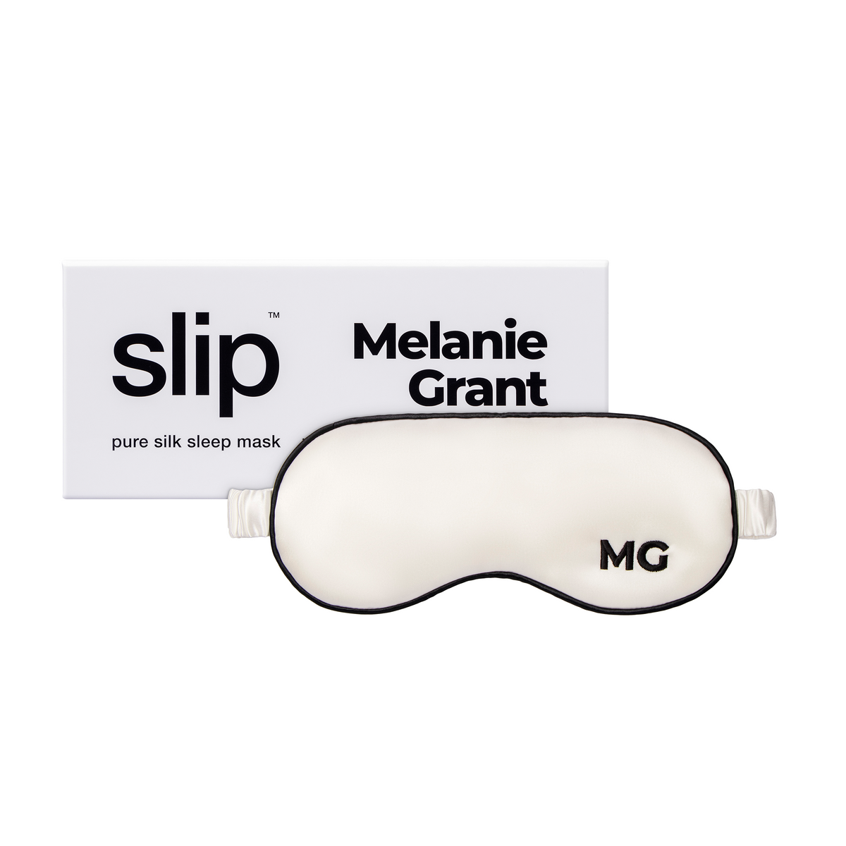 A white silk sleep mask with the initials 'MG' embroidered on the front, next to the box it comes in