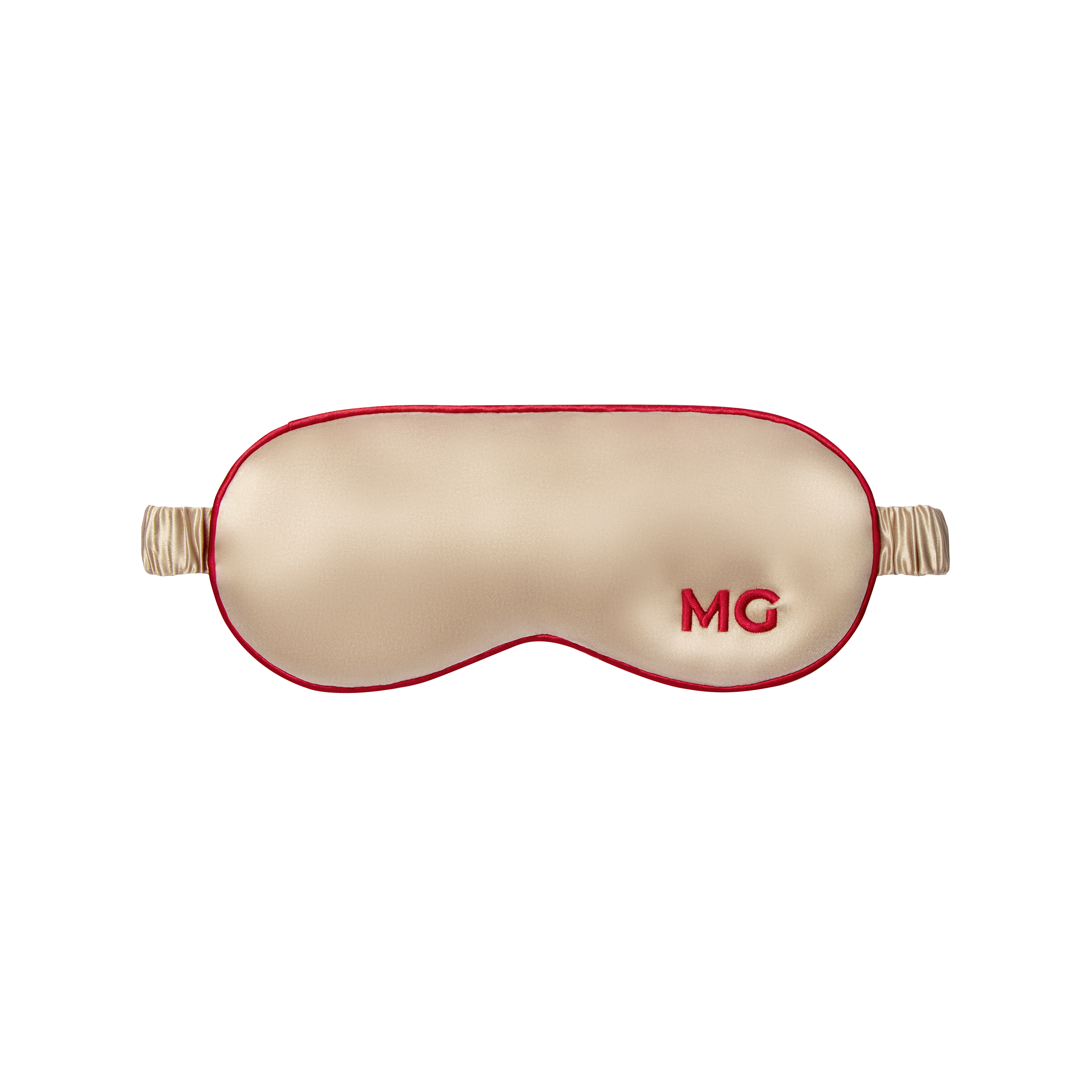 A champagne silk sleep mask with the initials 'MG' embroidered on the front.