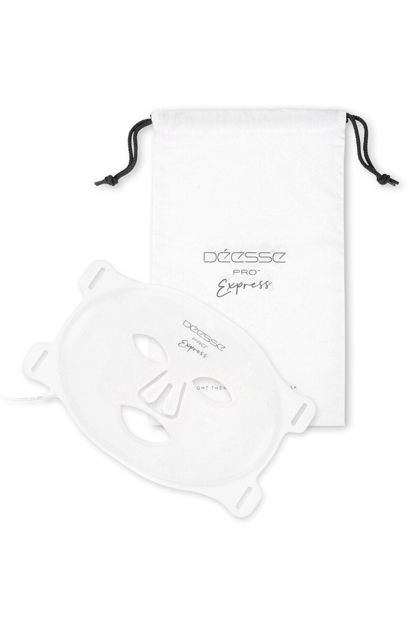 A silicone flexible LED light therapy mask by Déesse, displayed alongside a drawstring reusable bag, both are white in color.