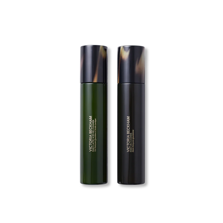 Two bottles of Victoria Beckham Beauty daily cleansing skincare products, one labeled as 'The Daily Oil Cleanser' and the other as 'The Daily Lactic Acid Gel Cleanser'.